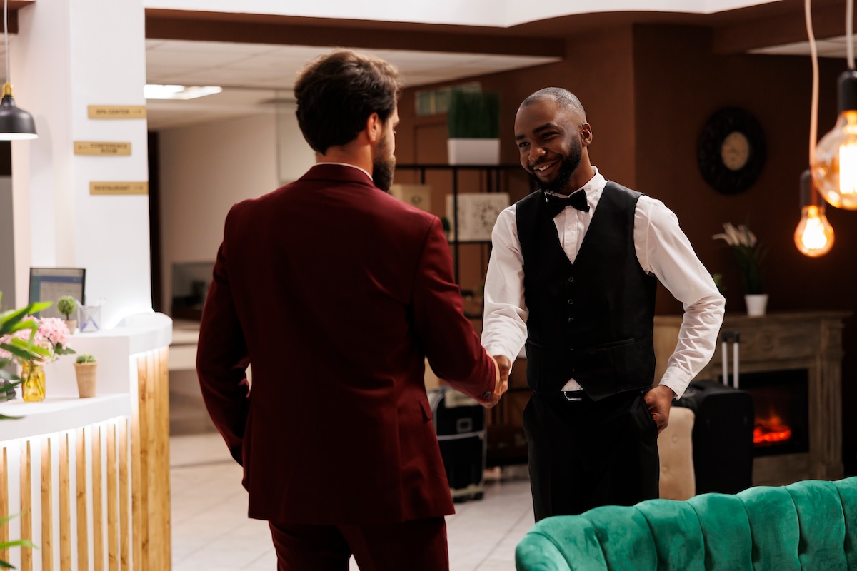 Diverse men shaking hands at hotel, african american concierge welcoming guest and offering his services. Bellhop provides excellent amenities to enhance business trip experience.